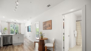 A modern kitchen with a central island, a dining area with a round table and chairs, and a hallway leading to a bathroom. - King Bed + Balcony Walk to Ponce City Market & BeltLine in Atlanta (Atlanta)