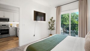 A modern bedroom with a bed, a TV mounted on the wall, a balcony with a chair, and a kitchen area. - King Bed + Balcony Walk to Ponce City Market & BeltLine in Atlanta (Atlanta)