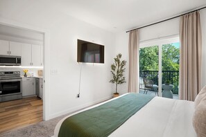 Ein modernes Schlafzimmer mit Bett, Wandfernseher, Balkon mit Stuhl und Küchenzeile.