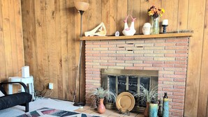 Ein Wohnzimmer mit einem Kamin aus Backstein, Holzvertäfelung, einem gemusterten Teppich und verschiedenen Dekorationselementen.