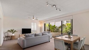 Una sala moderna con un sofá gris, una mesa de comedor de madera y un ventilador de techo.