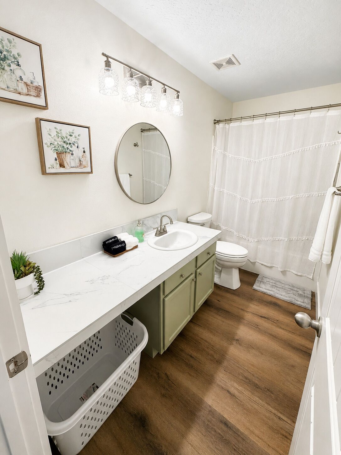 Une salle de bain avec un lavabo, un miroir et des toilettes blancs, un plancher en bois et un rideau de douche.