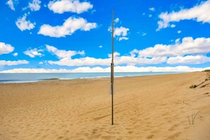 A beach with a vertical pole in the sand, a clear sky, and a calm sea in the background. - Surfside Rendezvous - Semi-oceanfront  with ocean views, easy beach access, and deck (Nags Head)