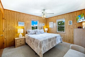 Een slaapkamer met een bed, nachtkastjes, een plafondventilator en ingelijste foto’s aan de wand.