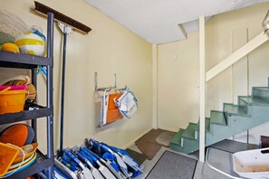 A laundry room with shelves, a broom, and a staircase. - Surfside Rendezvous - Semi-oceanfront  with ocean views, easy beach access, and deck (Nags Head)