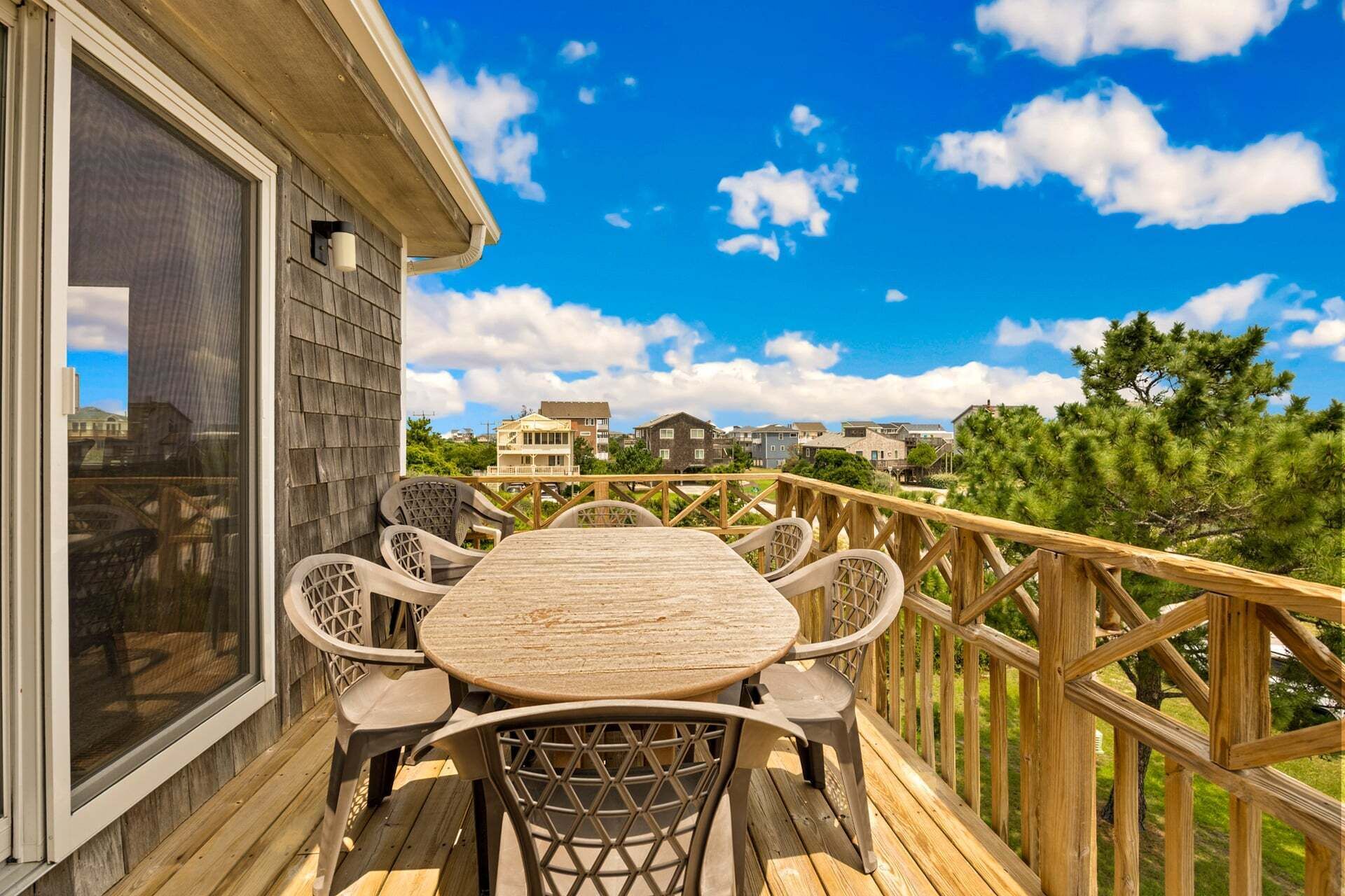 Una terraza de madera con una mesa y sillas, con vista a una zona residencial con casas y árboles.