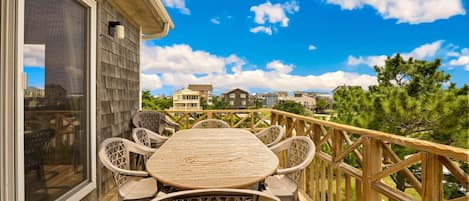 A wooden deck with a table and chairs, overlooking a residential area with houses and trees.