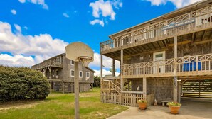 A wooden building with a basketball hoop, a balcony, and a sign that reads 'Surfside Rendezvous.' - Surfside Rendezvous - Semi-oceanfront  with ocean views, easy beach access, and deck (Nags Head)