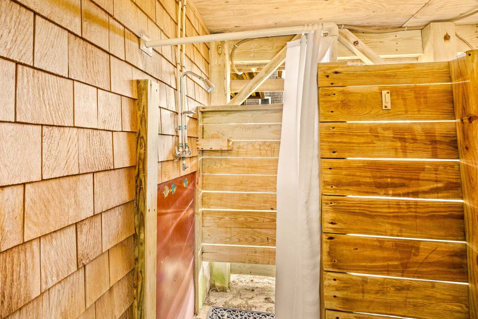 A wooden barn with a metal gate, a metal water spigot, and a red plastic barrier.