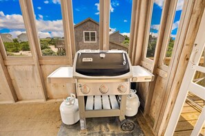 Ein mobiler Weber-Grill mit zwei Propangasflaschen, aufgestellt in einer Holzkonstruktion mit Blick auf Häuser im Hintergrund.