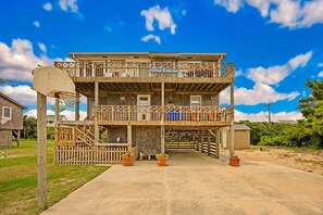 A two-story wooden building with a basketball hoop, a sign reading 'Surfside Rendezvous,' and a small porch area with potted plants. - Surfside Rendezvous - Semi-oceanfront  with ocean views, easy beach access, and deck (Nags Head)