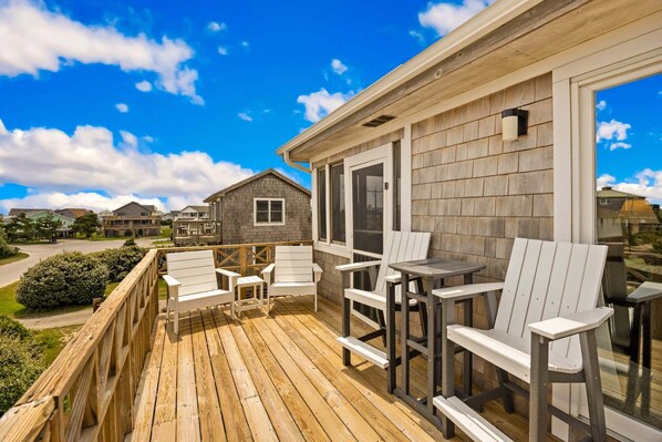 A wooden deck with outdoor seating, a view of neighboring houses, and a clear sky. - Surfside Rendezvous - Semi-oceanfront  with ocean views, easy beach access, and deck (Nags Head)