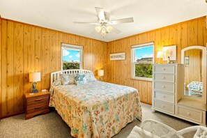 Ein Schlafzimmer mit Holzwänden, einem Bett mit floralem Bettbezug, einem Nachttisch, einer Kommode und einem Deckenventilator.