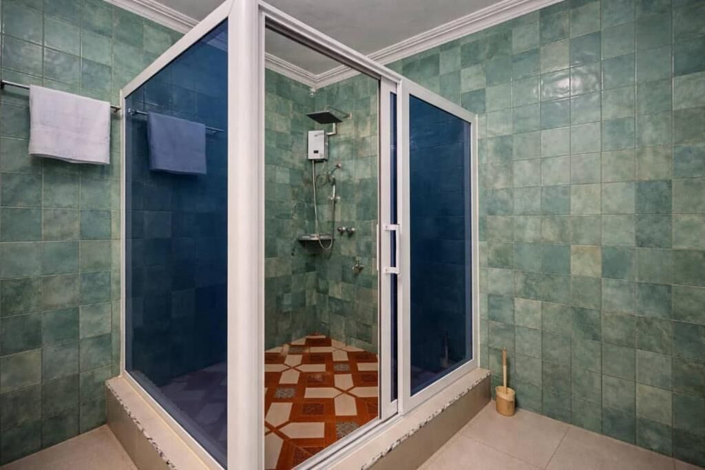 A bathroom with a glass-enclosed shower, green tiled walls, and a patterned floor.