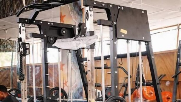 Un gimnasio con equipo de levantamiento de pesas, incluyendo una jaula de sentadillas, bancos y barras.