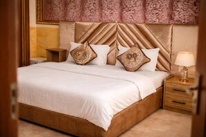 Una habitación de hotel con una cama grande, una mesita de noche, una lámpara y un cabecero estampado.