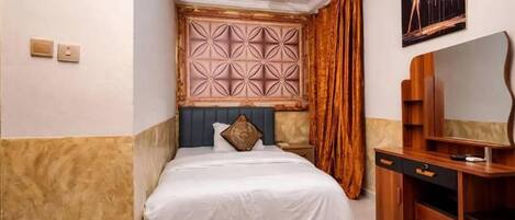 A bedroom with a bed, a desk, a ceiling fan, a wall-mounted TV, and a decorative headboard.