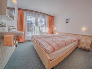 Ein Hotelzimmer mit einem Bett, einem Nachttisch, einer Lampe und einem Fenster mit Vorhängen. Es gibt ein Badezimmer mit Waschbecken und Handtuchhalter.