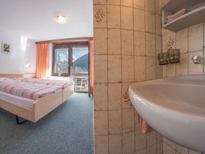 A hotel room with a bed, a bathroom with a bathtub, and a view of mountains through the window. - Bergrose Appartement/Fewo 5-Bettwohnung Nr. 2 by Interhome (Saas-Fee)