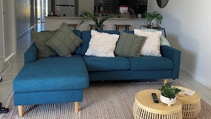 A modern living room with a blue sectional sofa, a woven rug, and a round wooden coffee table. - Bunker Down in Beautiful Bargara pet friendly on the Fraser Coast of Queensland (Bargara)