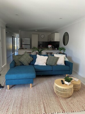 Ein stilvolles Wohnzimmer mit einem blauen Ecksofa, einem gewebten Teppich und einem runden Couchtisch aus Holz.