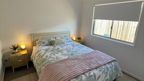 A bedroom with a bed, nightstands, a ceiling fan, a window, and a bedside lamp. - Bunker Down in Beautiful Bargara pet friendly on the Fraser Coast of Queensland (Bargara)