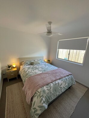 Ein Schlafzimmer mit Bett, Nachttischen, Deckenventilator, Fenster und einer Nachttischlampe.