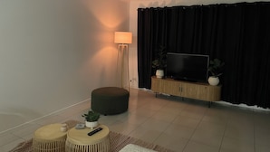 A living room with a ceiling fan, a flat-screen TV on a wooden cabinet, a floor lamp, two round ottomans, and a small potted plant. - Bunker Down in Beautiful Bargara pet friendly on the Fraser Coast of Queensland (Bargara)
