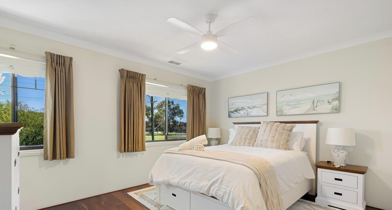 A bedroom with a bed, bedside tables, a ceiling fan, and artwork on the wall.