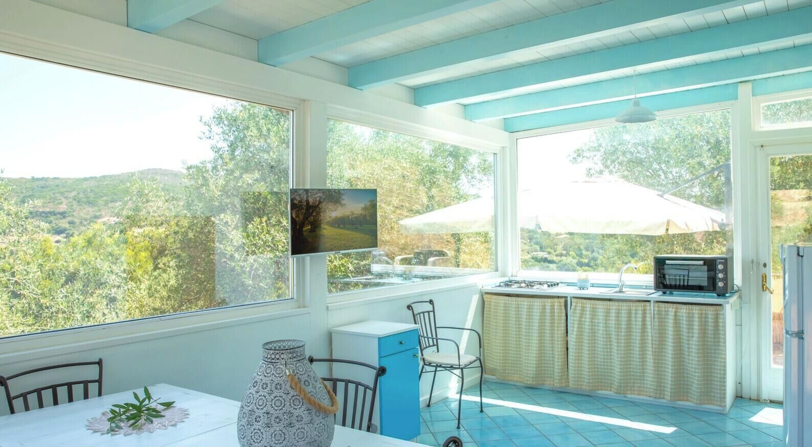 A kitchen with a view of the countryside, a dining table with chairs, a blue cabinet, and a microwave.