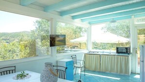 A kitchen with a view of the countryside, a dining table with chairs, a blue cabinet, and a microwave. - Casa Valverde, Alghero (Alghero)