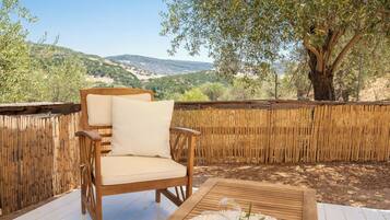 A wooden deck with a wicker chair and a table, overlooking a mountainous landscape.