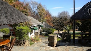 A stone-paved courtyard with thatched-roof structures, a wooden table, and chairs. - Premier Hotel Himeville Arms (Himeville)