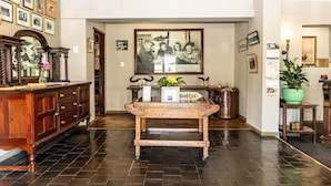A reception area with a wooden reception desk, framed pictures on the walls, and a large painting above the desk. - Premier Hotel Himeville Arms (Himeville)