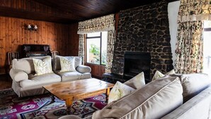 A cozy living room with a stone fireplace, wooden walls, and a patterned rug. - Premier Hotel Himeville Arms (Himeville)