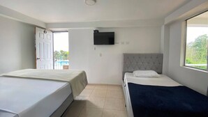 Habitación de hotel con dos camas, televisión y ventana con vistas a zonas verdes.