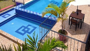 Piscina rectangular con azulejos azules y diseño de cuadros, rodeada por un suelo de piedra y barandilla de metal.