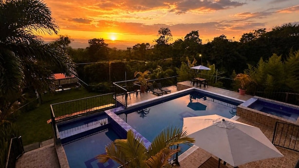 Piscina con vista al atardecer, rodeada de follaje y un pequeño patio.