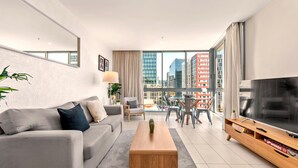 En moderne stue med sofa, sofabord, fjernsyn og udsigt over byen.