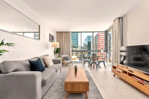 Ein modernes Wohnzimmer mit Sofa, Couchtisch, Fernseher und Blick auf die Stadt.