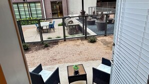 Un balcón con mobiliario exterior, una pequeña mesa con una planta y vistas a un edificio con varias ventanas y un muro de ladrillo.