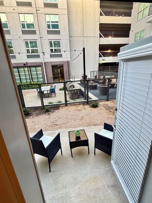 Ein Balkon mit Gartenmöbeln, ein kleiner Tisch mit einer Pflanze und Blick auf ein Gebäude mit vielen Fenstern und einer Backsteinmauer.