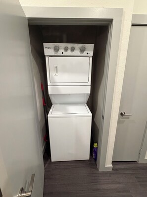 A compact laundry room with a Whirlpool washer and dryer, a door with a handle, and a wooden floor. -  Pet-Friendly Heights 1BR,Pool, Gym, Pet Spa, Free Parking (Houston)