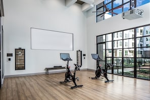 Ein großzügiger Innenbereich mit großen Fenstern, Trainingsrädern und einer leeren Projektionsleinwand.