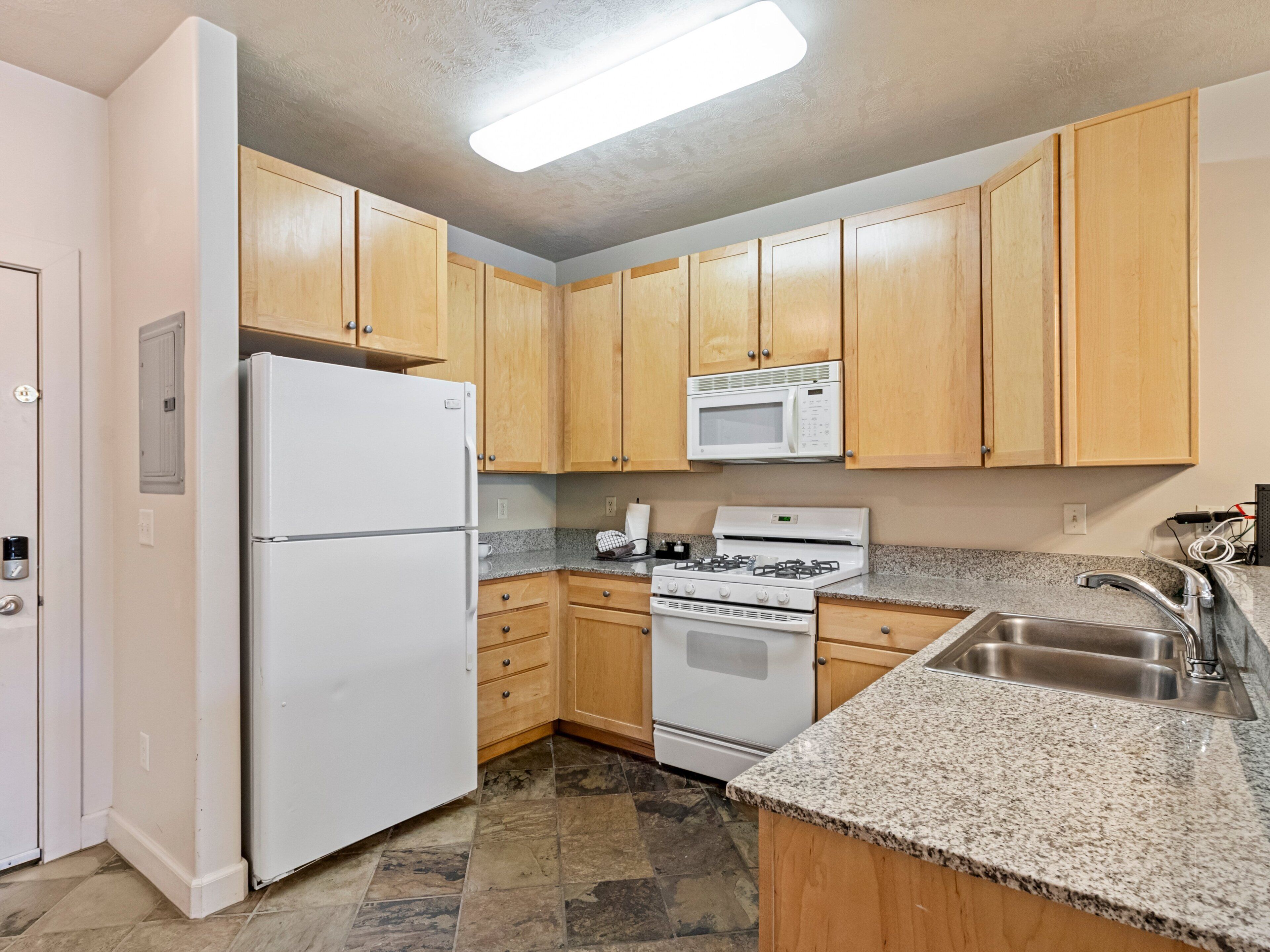 A kitchen with wooden cabinets, a white refrigerator, a microwave, a stove, and a granite countertop.