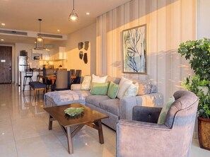 A modern living room with a sofa, armchair, and coffee table. There is a dining area with chairs and a table, and a kitchen in the background. - Spectacular "Camino al Mar" for 6 people (Mazatlán)