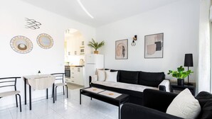 Una sala de estar moderna con un sofá negro, una mesa de comedor y una cocina al fondo.