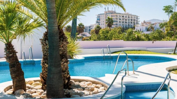 Una piscina rodeada de palmeras y un edificio al fondo.