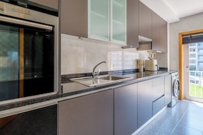 Eine moderne Küche mit Einbauofen, Spüle aus Edelstahl und Fenster mit Blick auf eine Wohngegend.