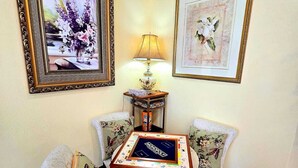 A room with a Monopoly board game on a table, two chairs with floral cushions, a lamp, and two framed pictures on the wall.